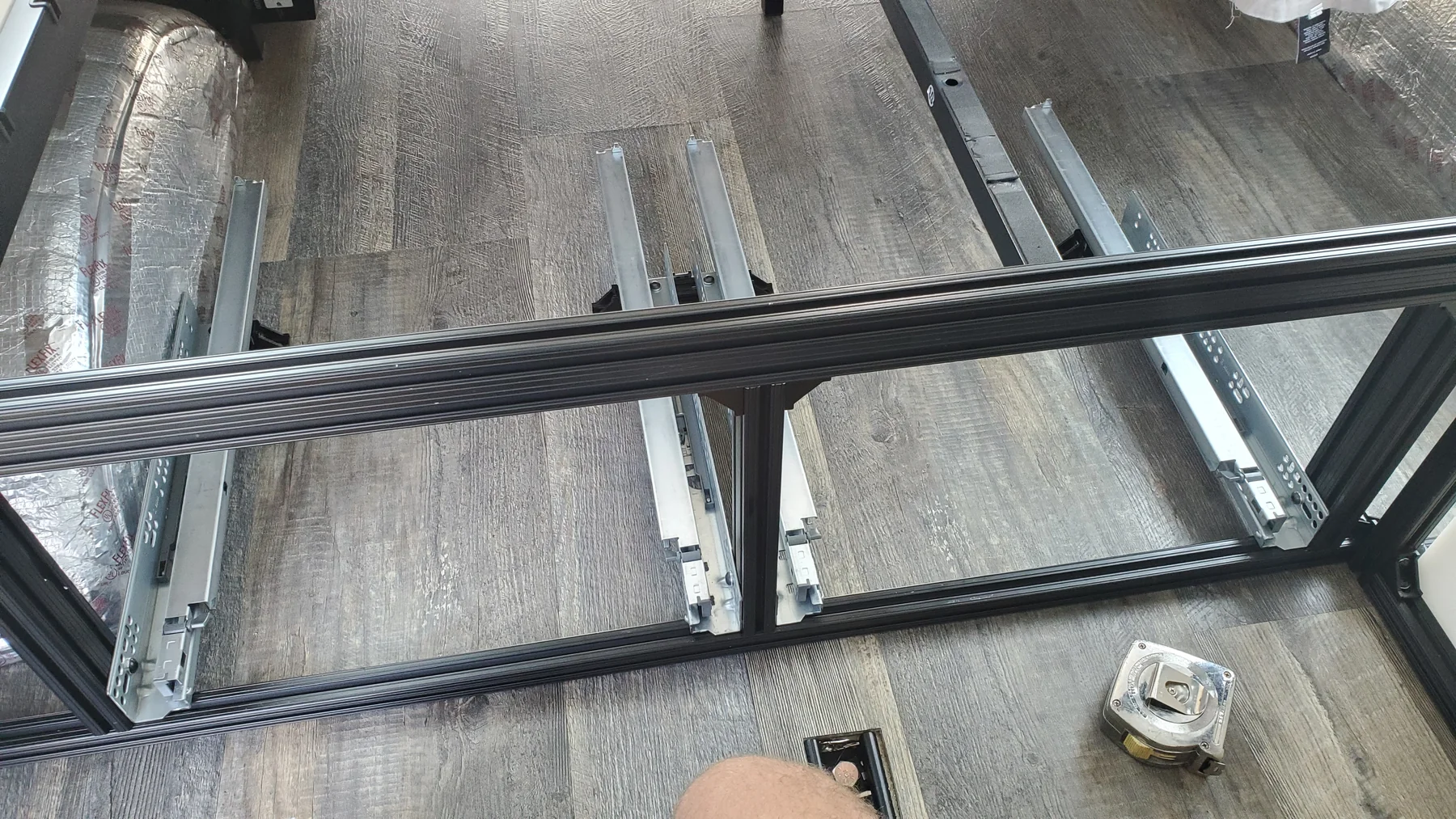 Black slotted frame dividing two under-bed storage bays, with low metal drawer runners exposed.
