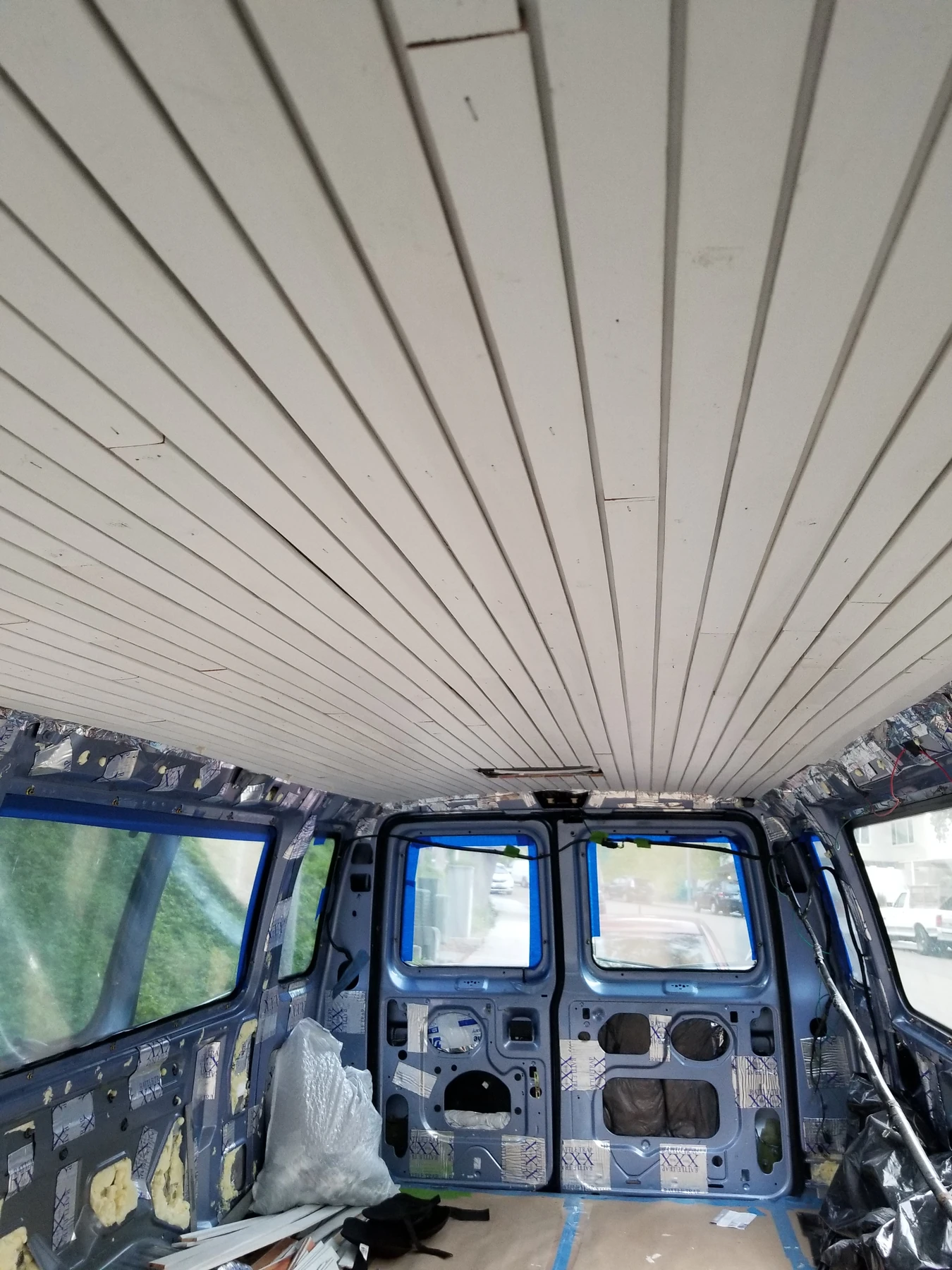 Narrow white grooved ceiling strips running lengthwise above the unfinished van interior.