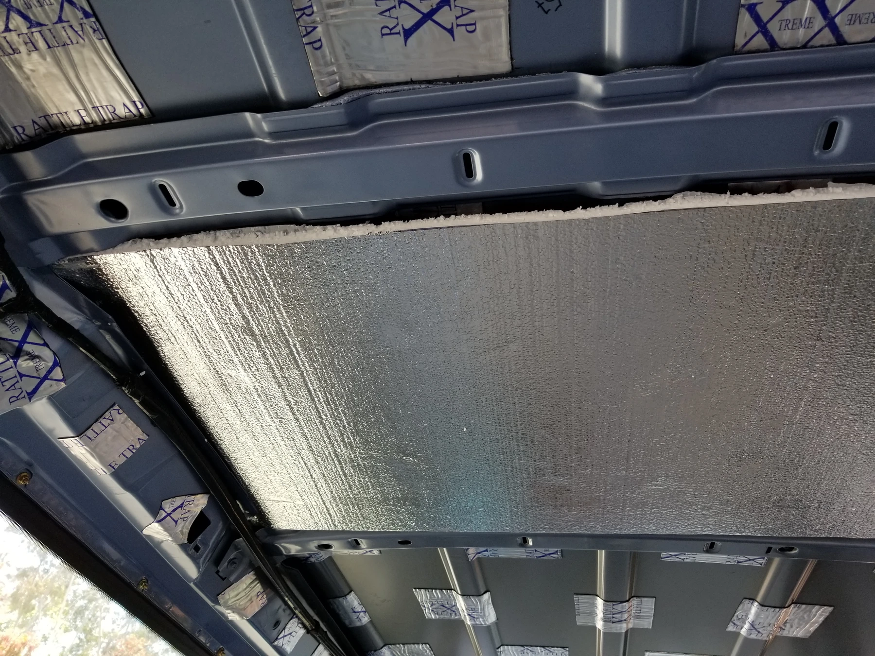 Pale foil-faced rigid panel between van roof ribs, beside exposed damping patches.