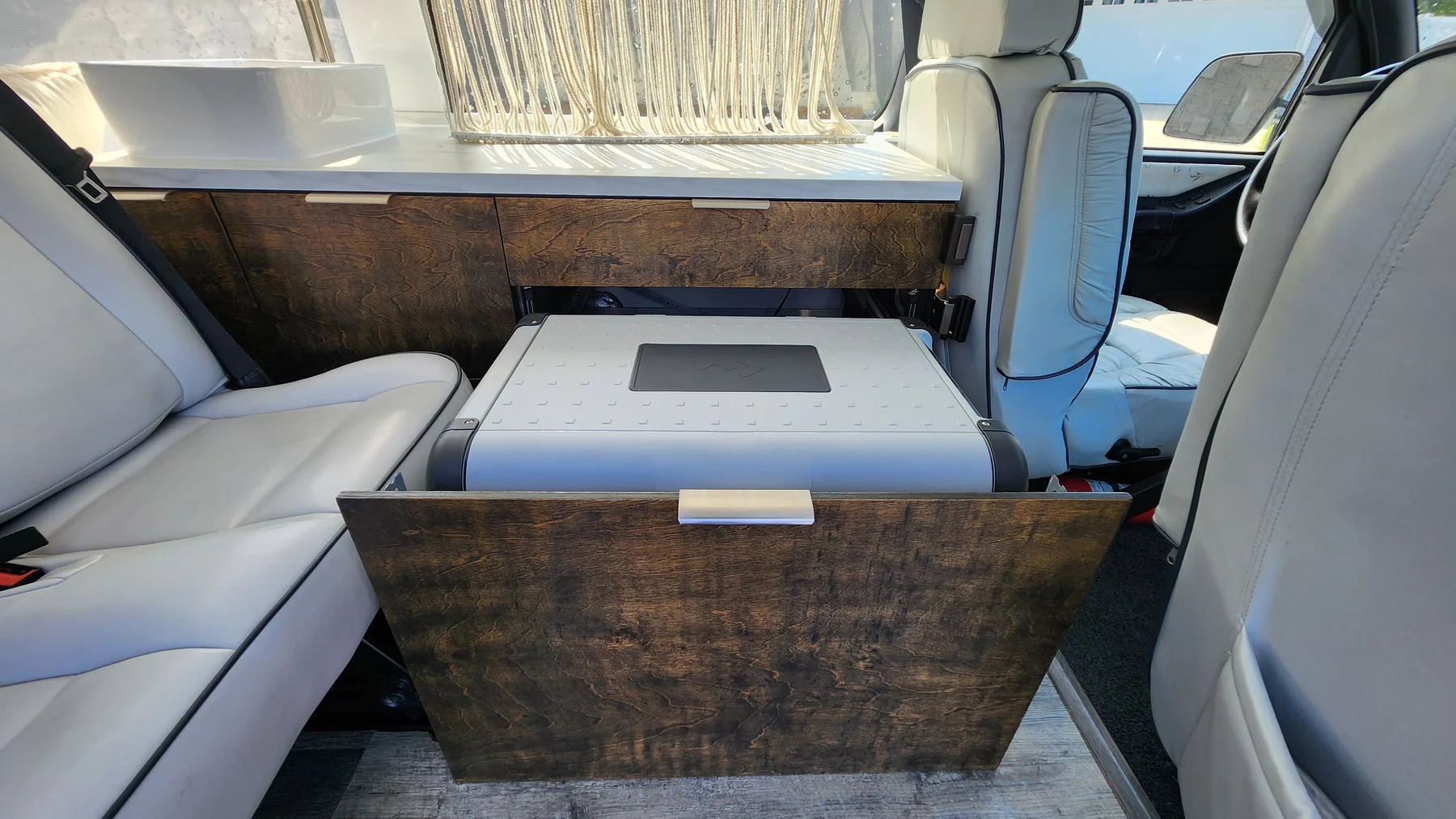 Dometic cooler on a pull-out tray below the kitchen counter between upholstered seats.