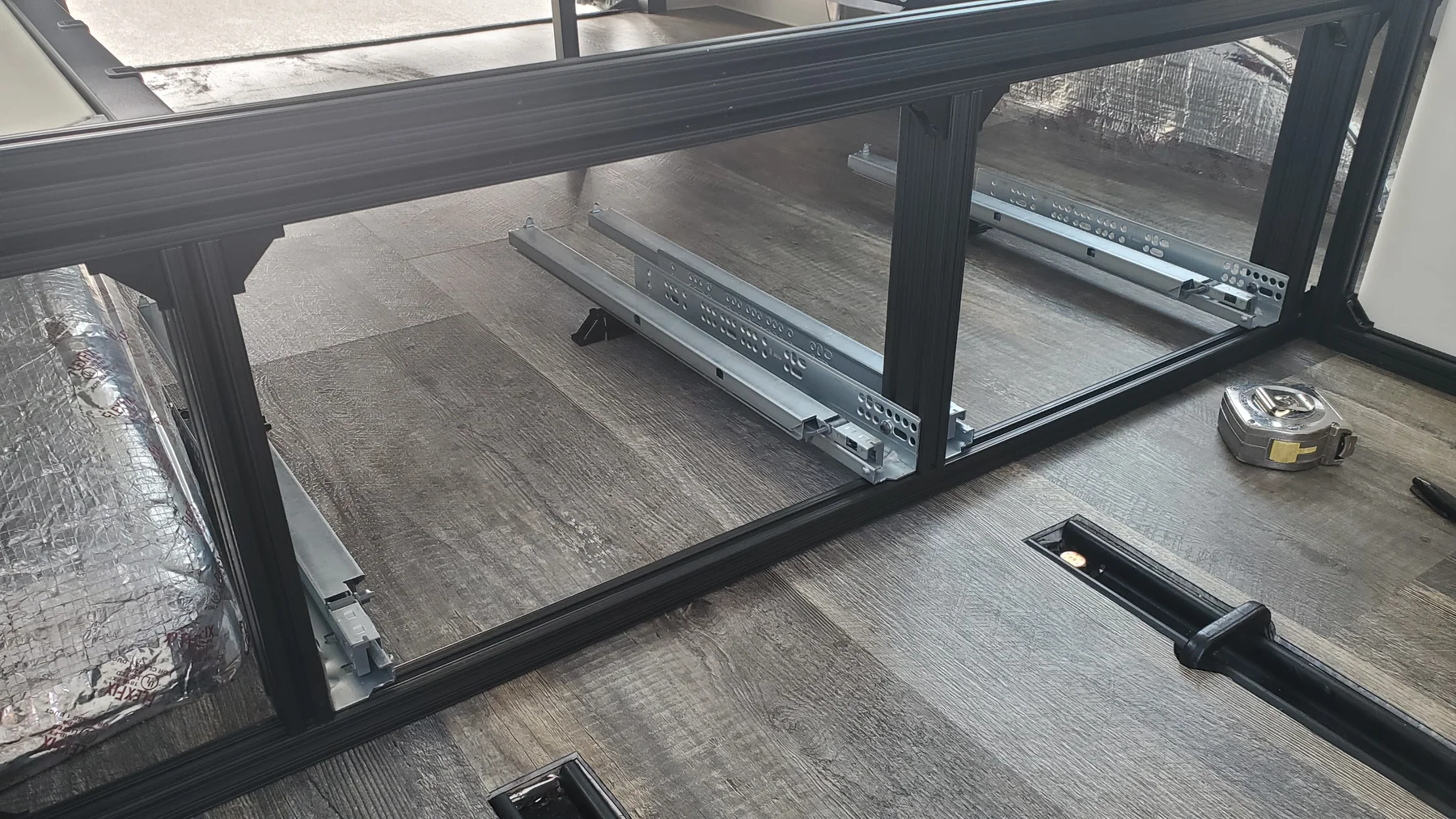 Two open bays in the bed frame showing paired low drawer runners and their mounting space.
