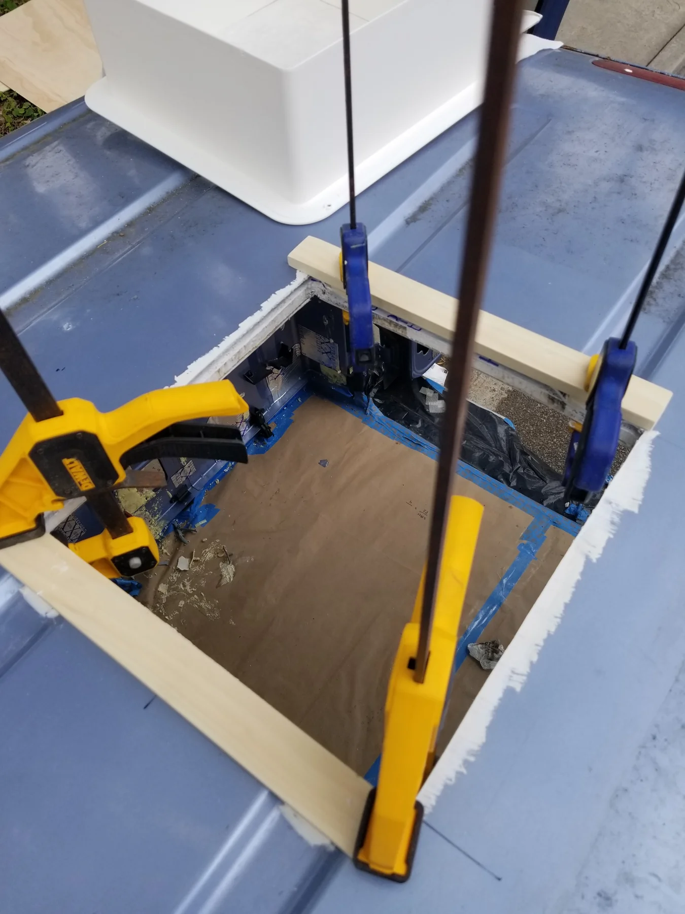 Long wooden pieces spanning a roof opening while clamps reach through it.