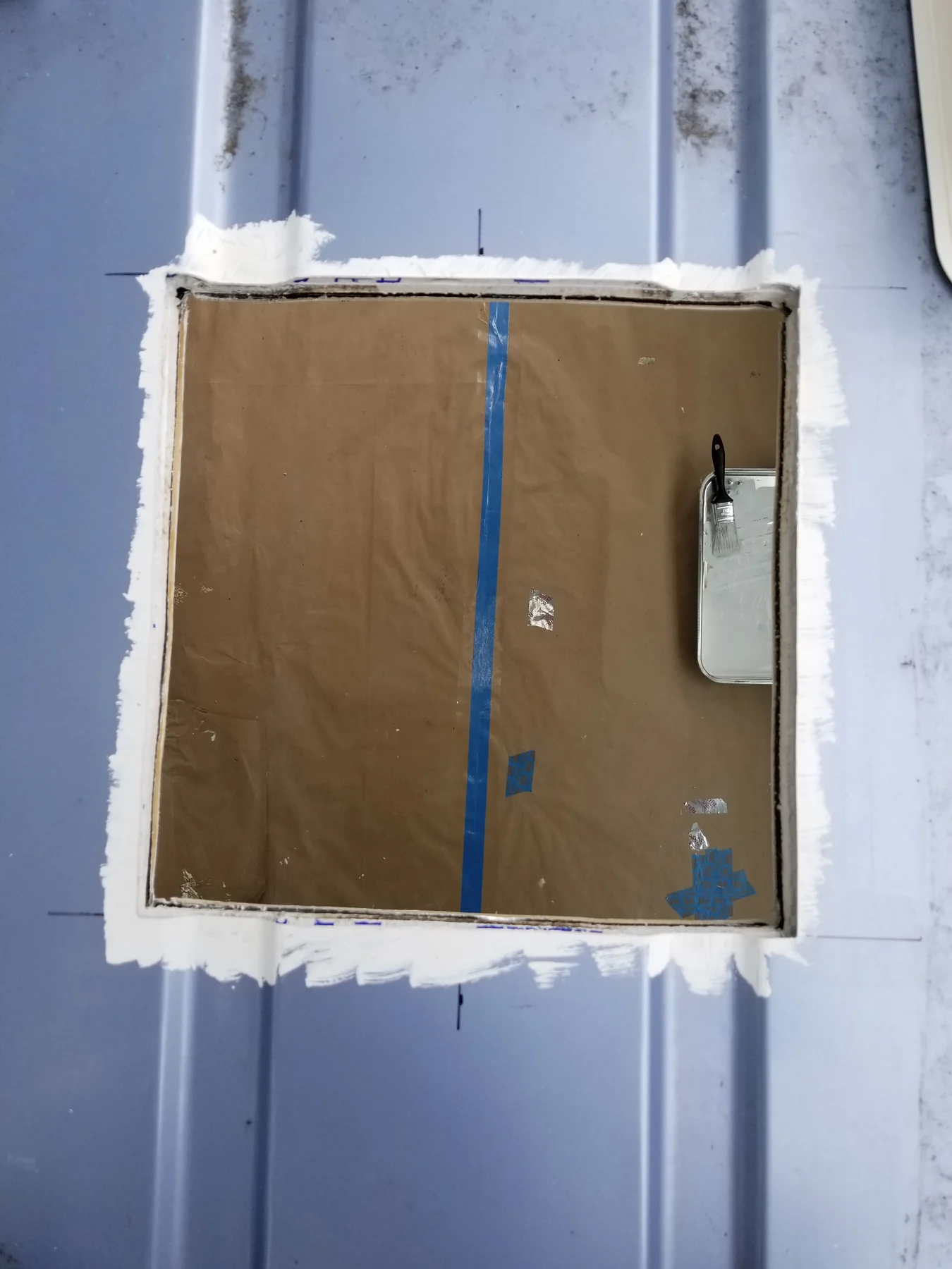 Square opening in Walter’s blue roof with white perimeter treatment and paper protecting the interior.