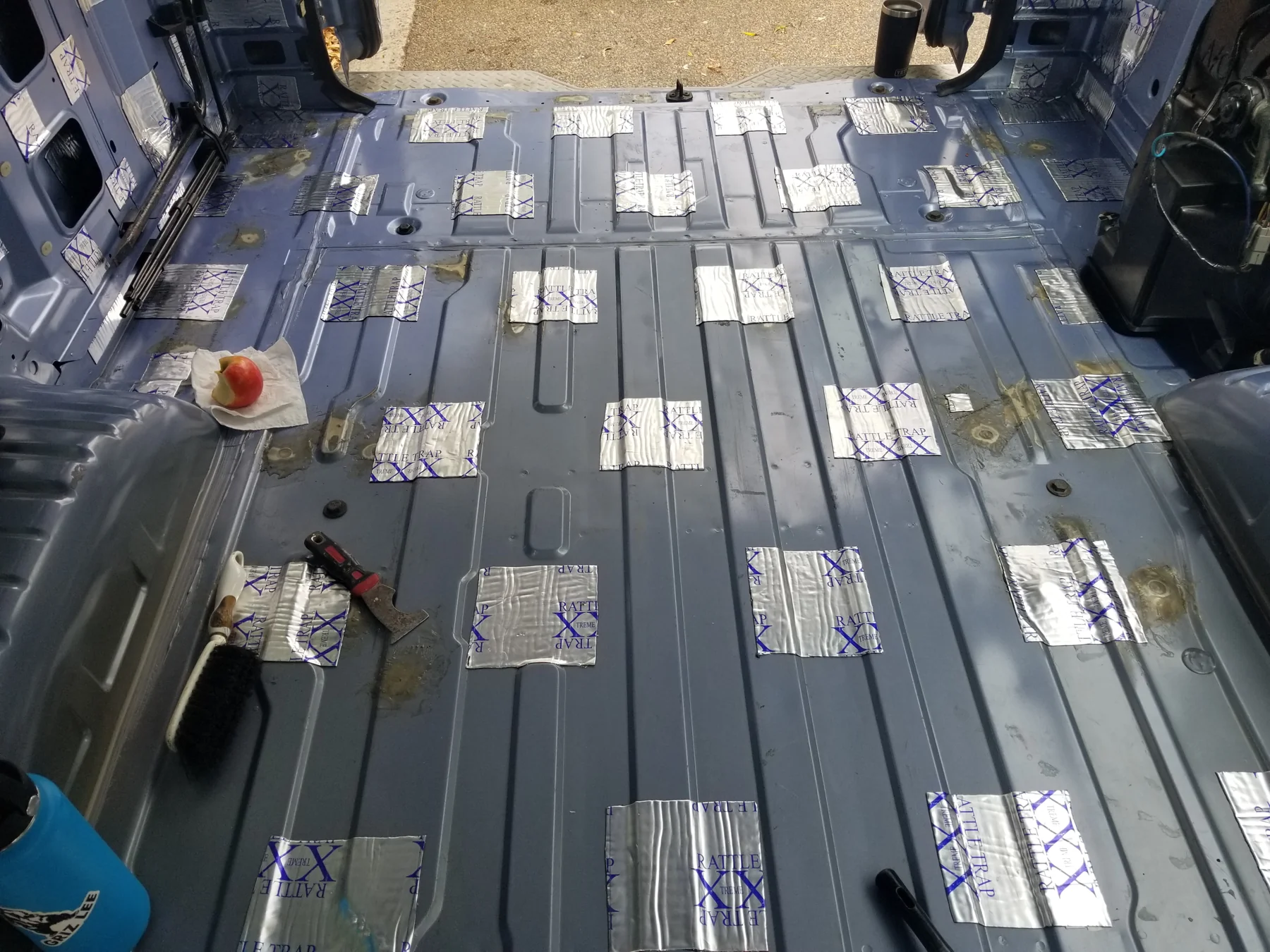 Blue ribbed van floor with separate foil-faced RattleTrap patches and exposed steel between them.