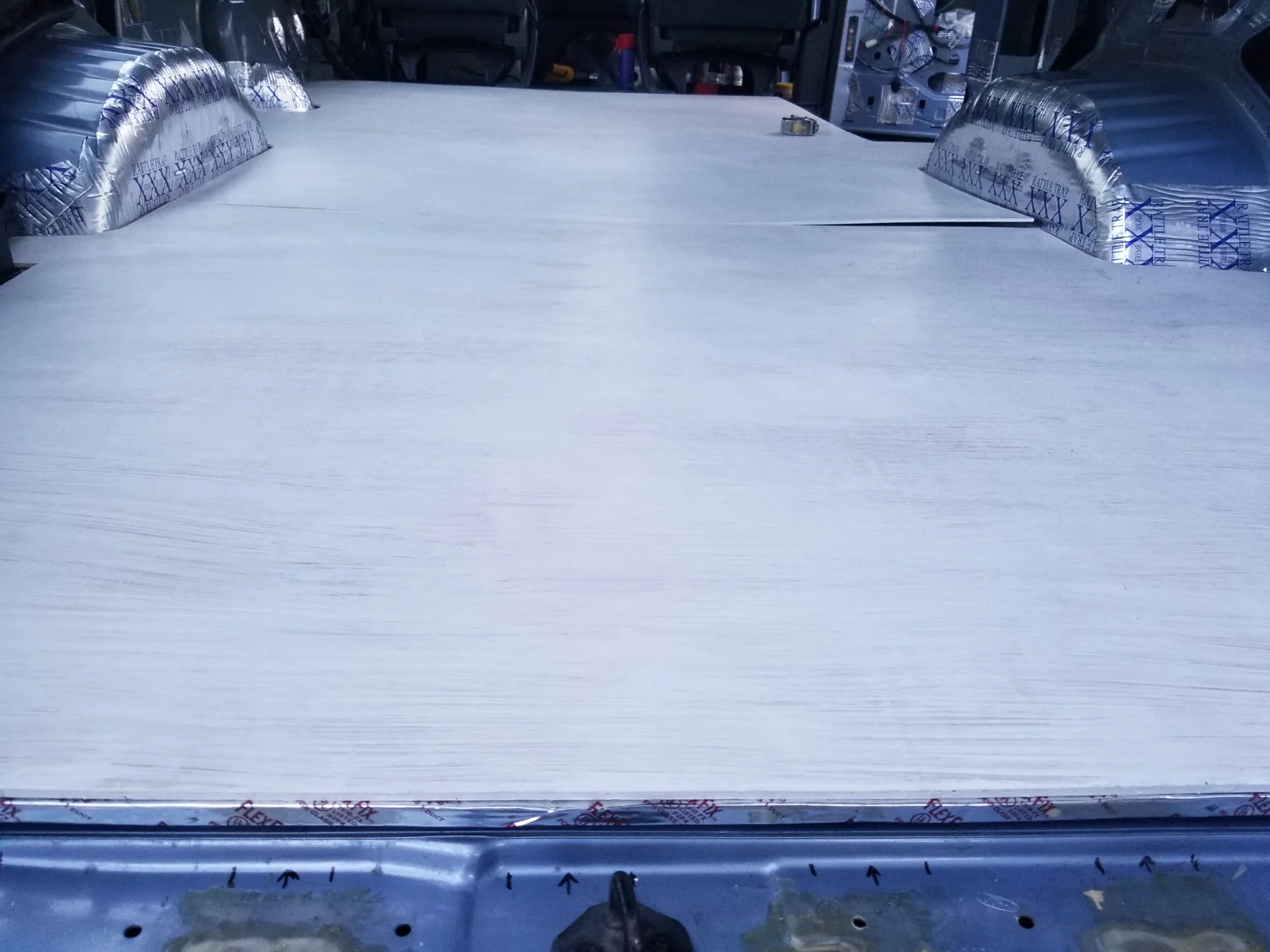 Pale floor panels with a transverse joint and shaped cuts around both rear wheel wells.