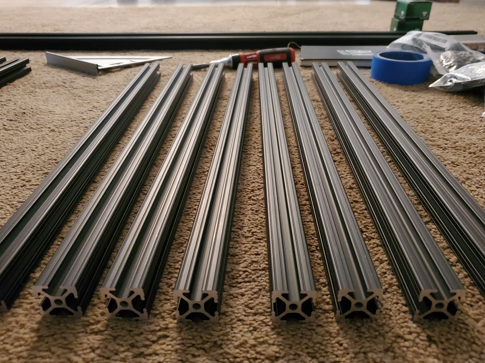 Dark slotted extrusion lengths laid on carpet, with exposed cross-sections and loose workshop parts.