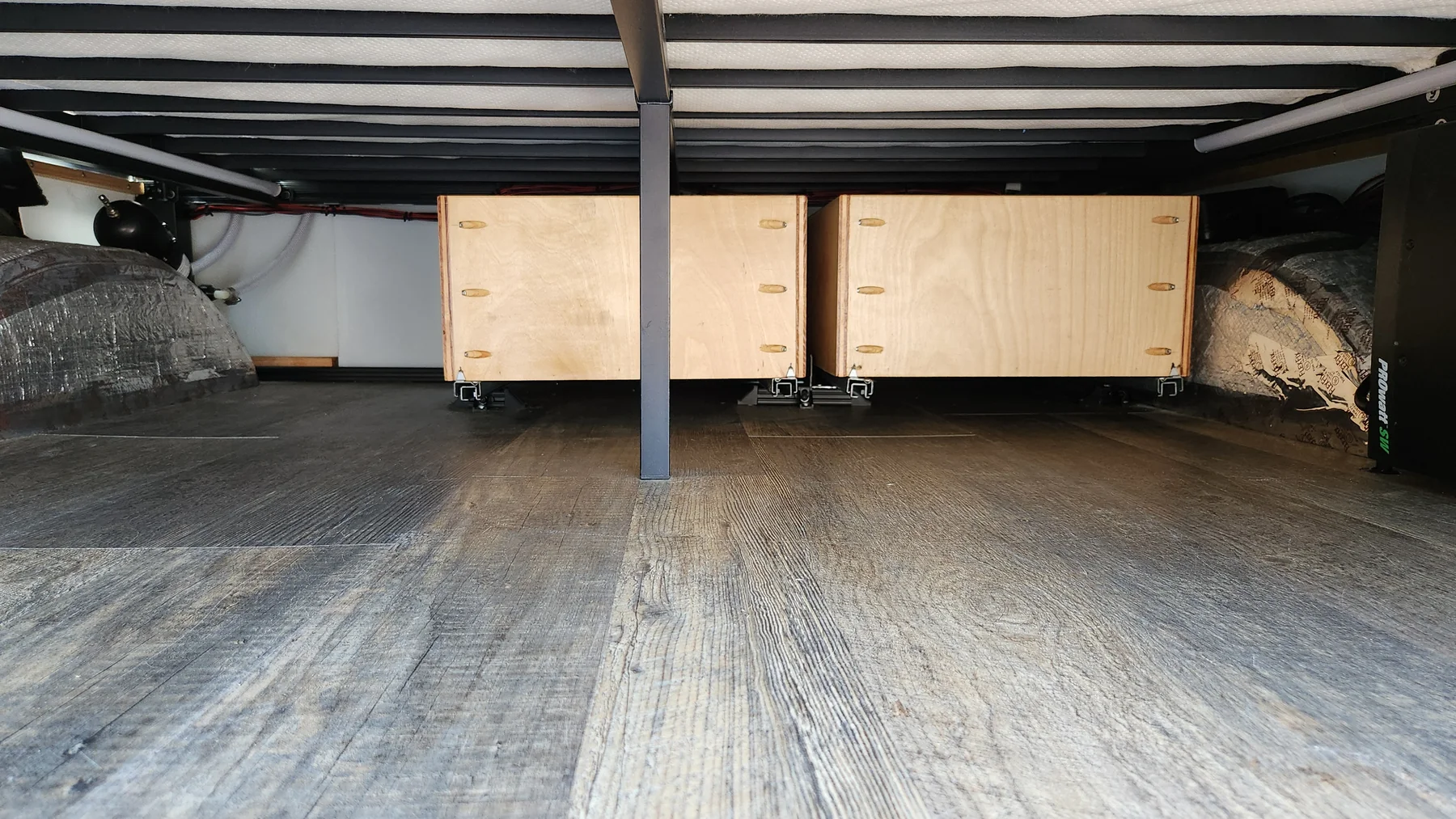 Rear garage below the campervan bed showing a central support, two drawer backs and pale slats overhead.