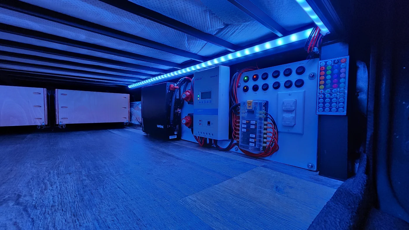 Blue LED lights illuminating the campervan’s under-bed storage and electrical controls.