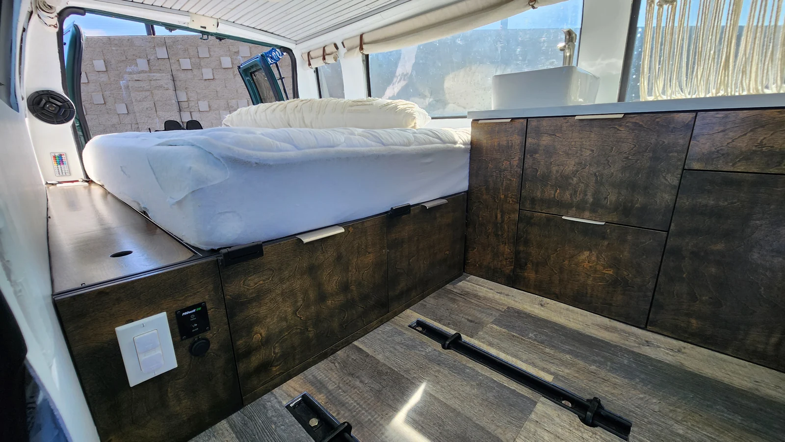 Finished campervan interior showing the bed platform, wood cabinets, sink and open floor.