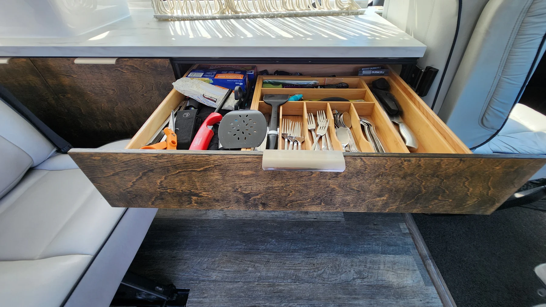 Wide kitchen drawer with wood organizer holding cutlery and cooking utensils beneath the counter.