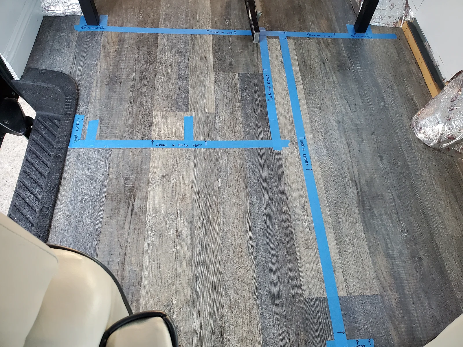 Blue tape lines and handwritten layout labels on the wood-pattern van floor.