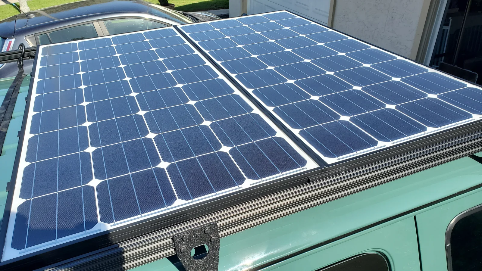 Two glass-front solar modules side by side between dark roof-rack rails.