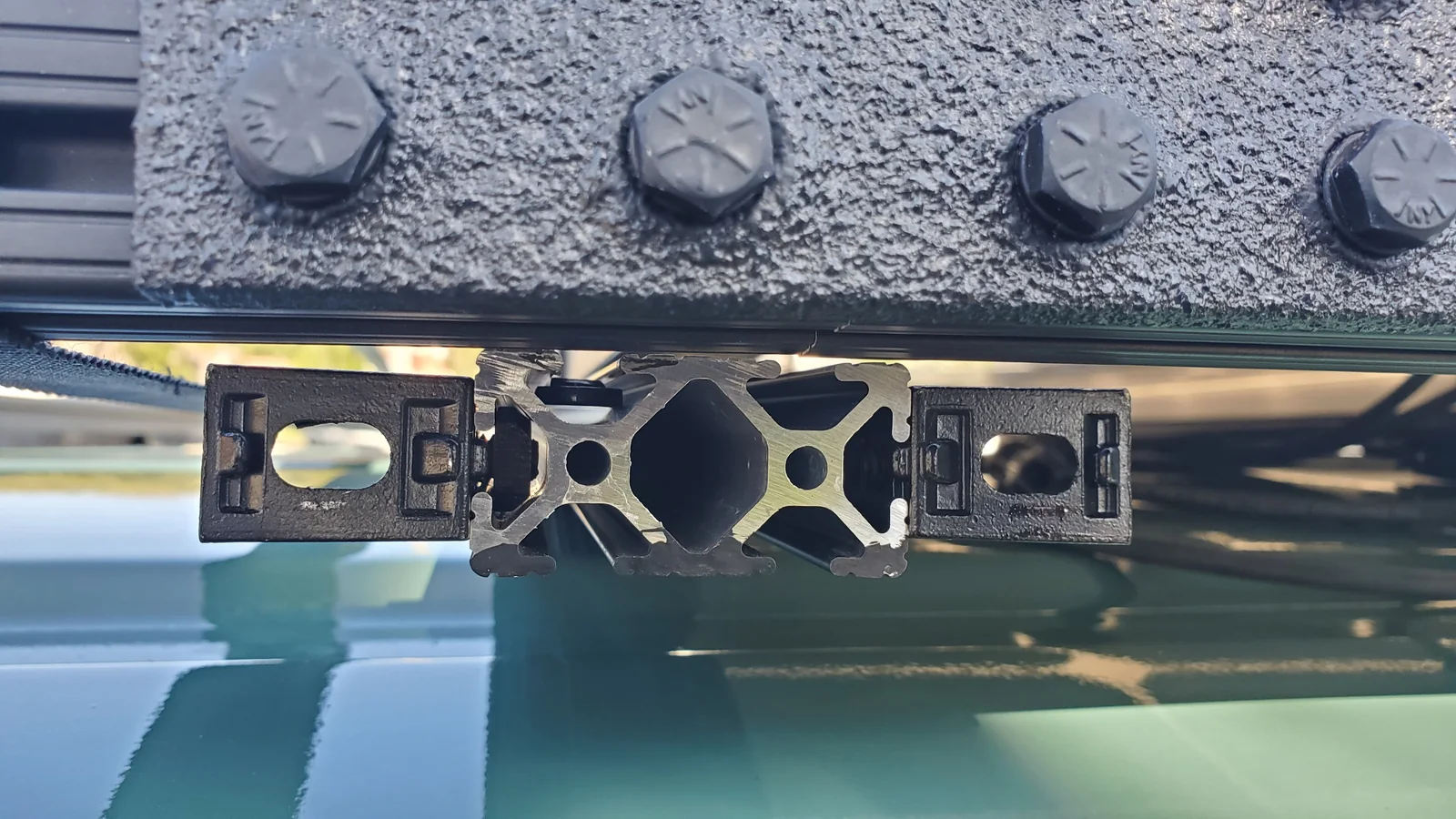 Close view of a roof-rack extrusion end beneath an upper member and textured mounting plate.