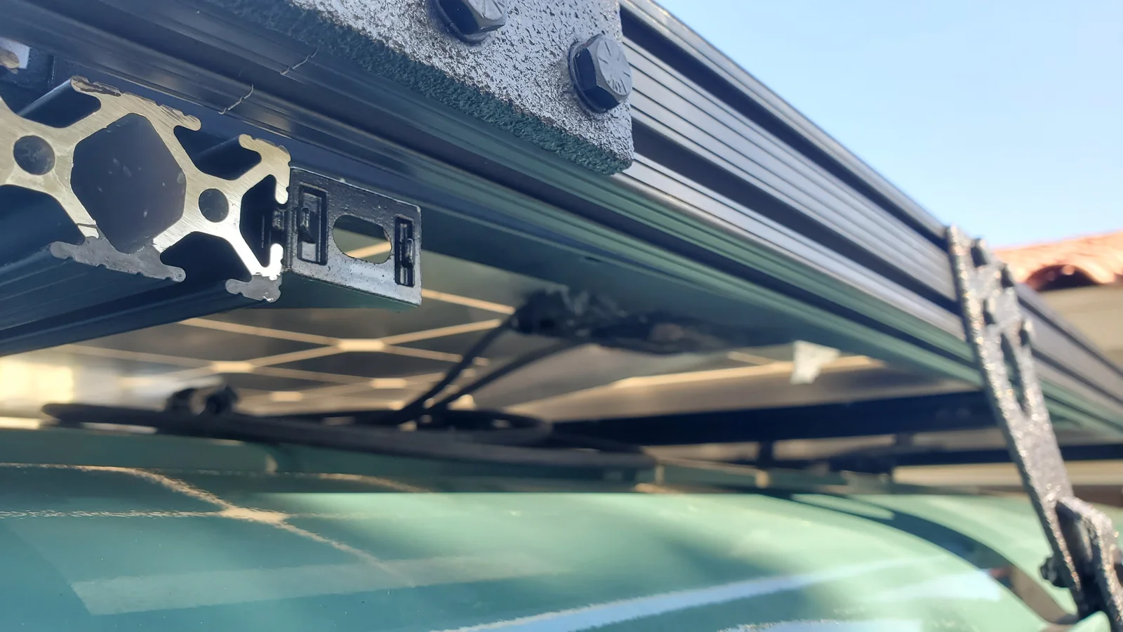 Angled underside view of roof-rack rails, solar panel backs and a support above the green roof.