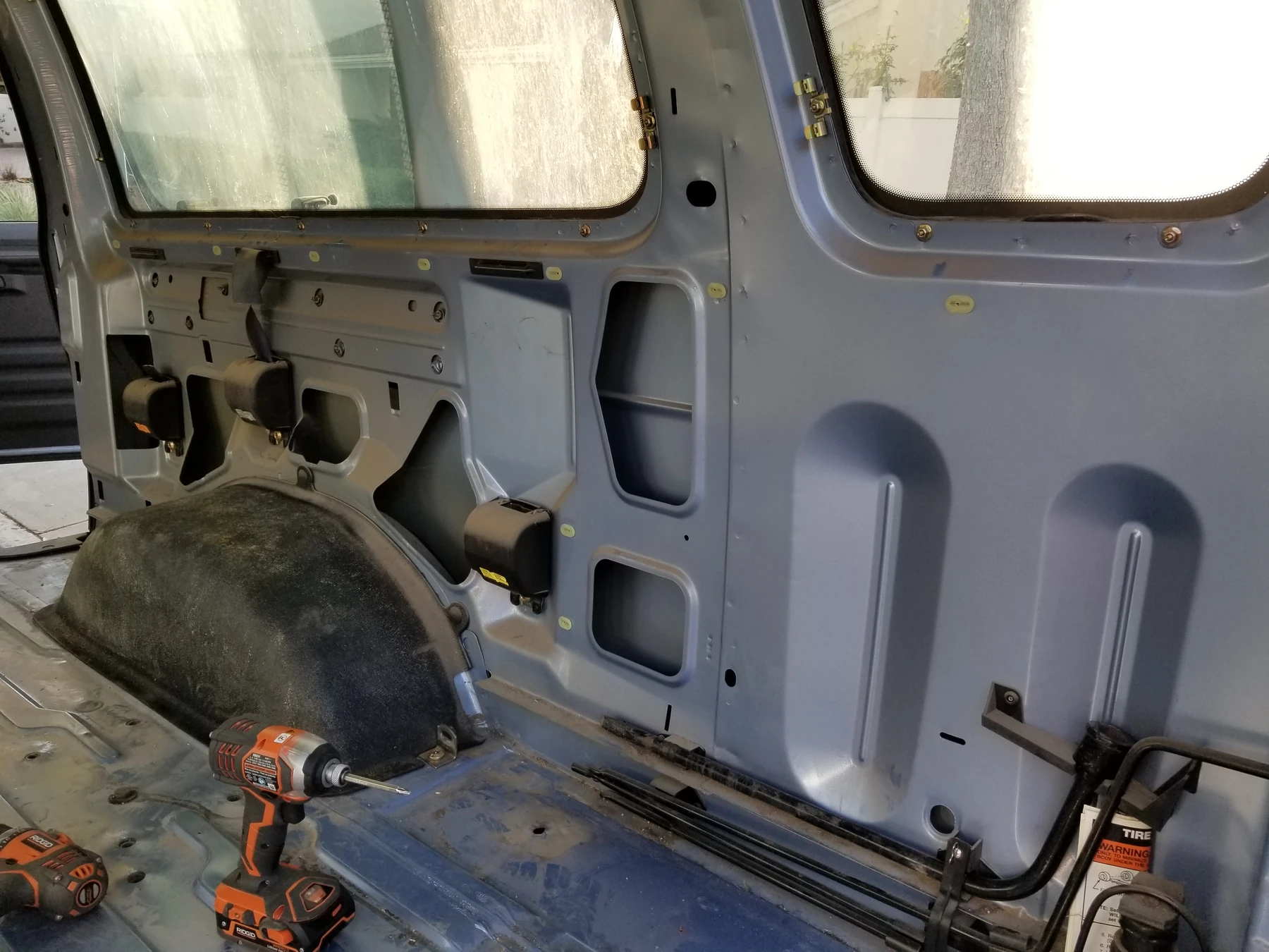 Bare stamped sidewall, openings and wheelwell above the exposed van floor.