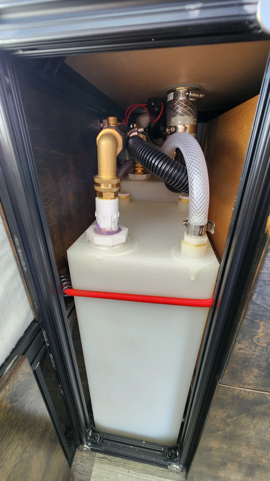 White water container in an open narrow cabinet bay, with red restraint cord and visible hoses above it.