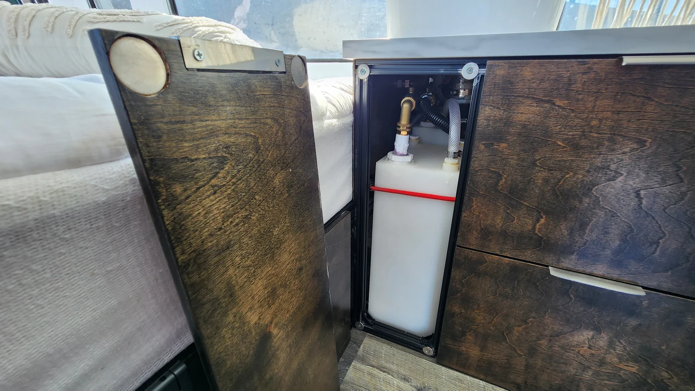 White water container and plumbing inside the kitchen cabinet.